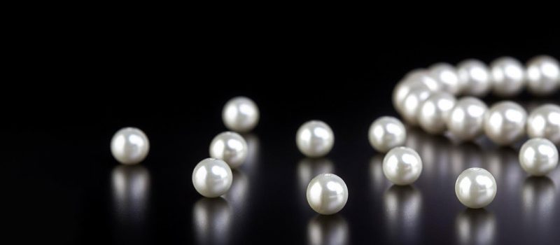 Pearl Jewellery Buying Guide White pearls in a string and loose on a black reflective background
